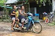 Girl riding a motorcycle with two passengers laughing on the muddy slope of Don Khon.