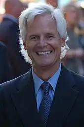 A man with white hair is looking and smiling at the camera.