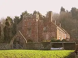 Red brick building with tall chimneys. In the foreground is an arcjed gateway.