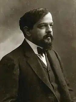 A man with a beard and moustache facing right wearing a black jacket and bow tie.