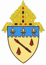 The arms of the Diocese of Baton Rouge: The shield features a red baton, referencing the city name, Baton Rouge, Louisiana, and its literal French meaning.