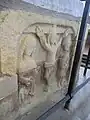 Crucifixion scene, sculpted in low relief on west end of base of chest tomb of Sir William de Tracy (d.1322), cleric, incumbent of Mortehoe; South transept.