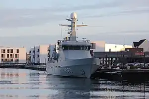 A grey warship docked alongside a wharf