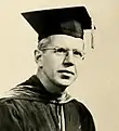 White male in academic dress wearing a mortarboard