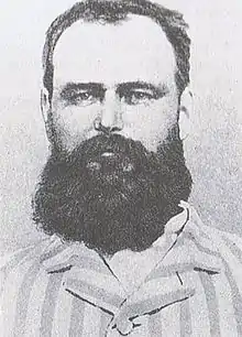 Black and white photograph of the head and shoulders of a bearded man wearing a striped top