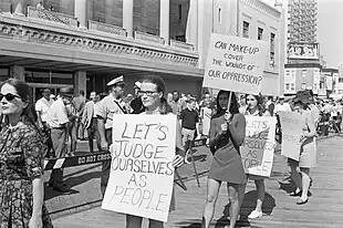 Women holding signs reading "Let's judge ourselves as people" and "Can make-up cover the wounds of our oppression?"