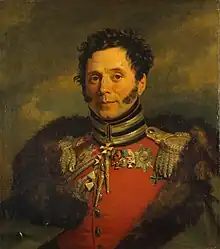 Painting of a smiling clean-shaven man with long sideburns. He wears a red military uniform with a fur-lined cloak thrown over his shoulders.