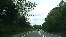 single-carriageway road with central double white lines and passing between trees