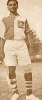 A Black and White photo of man holding hockey stick in his right hand.