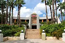 The gateway to a facility reading "Jurassic Park" at the top, "Discovery Center" at the bottom, and a rocky panel with a Tyrannosaurus skeleton in-between.