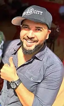 Abdelhafid ad Douzi wearing a gray shirt and ballcap, holding a thumbs-up, smiling at camera