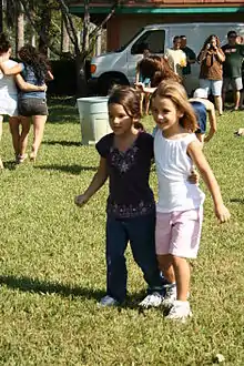 Two children stand side by side, connected by a tie at the ankle.