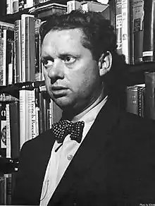 A black and white photograph of Thomas wearing a suit with a white spotted bow tie in a bookshop in New York.