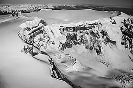 The flat-topped summit of a snow-covered mountain with a rocky and snow-covered cliff in the foreground.