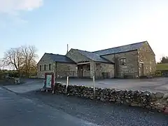 A sandstone building set in a small car park with a low sandstone wall surrounding the car park