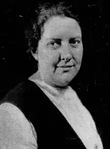 Portrait of a woman whose hair is pulled back and is wearing a dark v-necked frock over a white blouse