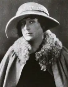 A white woman wearing a wide-brimmed hat and a cloak with a fur collar