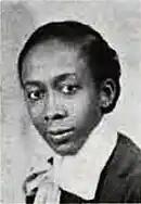 Portrait of a young black woman in a dark shirt with a wide white collar and bow at the neck