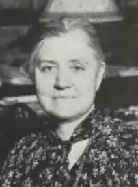 An older white woman with grey hair, wearing a print blouse or dress