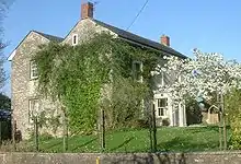 Gray stone building with slate roof, partially obscured by trees.