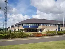 Two-storey office building made with facing brick, glass and dark blue cladding set in mature landscape