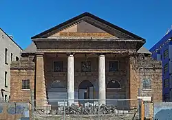 A small columned and pedimented church, derelict behind a chain link fence