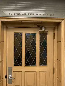 A photo of the door of the chapel in the Fitzsimons Building. Stained glass was installed in the door and also inside the chapel room. Scripture "Be still and know that I am God." Pslam 46:10, is found above the door.