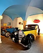 Photograph of a vaulted room containing two top-of-the-range cars from the inter-war period.