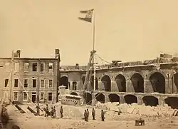 1861 photograph of the interior of a damaged military fortification. The flag of the Confederate States of America flies from a flagpole near the center of the photograph.