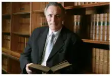 Frank Rivers in 2020 in front of a book shelf with a book in his hands