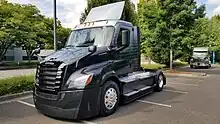 Black day cab Freightliner eCascadia. 3/4 view so you can see front and left side.