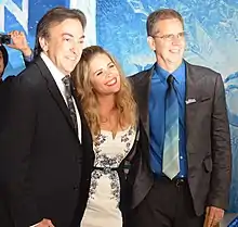 Three people smiling for a photograph before a Frozen-themed red carpet backdrop