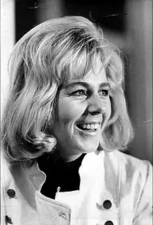 B&W portrait photo of a smiling blonde woman wearing a white coat with black buttons