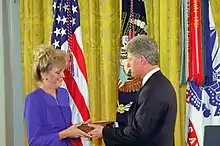 Man in suit hands item to woman in purple.