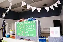 Room showing a multicolored scoreboard divided between "Team Pink" and "Team Blue" for a gender-reveal party.