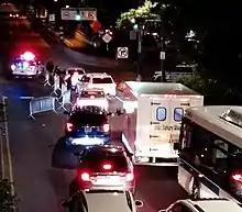 vehicular traffic merging lanes in front of a police checkpoint on Queensboro Plaza right before the Queensboro Bridge, which crosses into Manhattan; metal barriers reducing the roadway to one lane; police officers speaking to drivers before allowing passage; police cruisers nearby