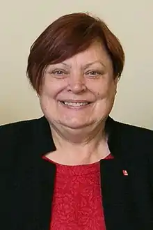 Head and shoulders photograph of a short-haired woman wearing a black suit coat and red blouse