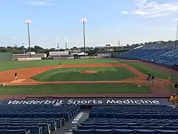 A view looking over the dirt and green grass of the infield as men rake the dirt and paint the lines before a game