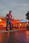 Gus's Giant Muffler Man, in front of a restaurant, with neons lit, dusk