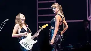 Haim and Taylor Swift in glamorous, grunge-inspired all-black outfits in a 2022 concert.