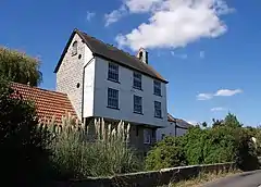 Tall house with upper story projecting above the ground floor and faced with white wooden boards.