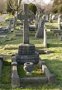 A granite headstone surmounted by a Celtic cross, among several other gravestones