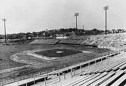 A black and white photograph of a baseball stadium in the final stages of construction, lacking infield dirt and warning track gravel