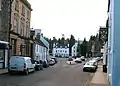 The Cross (the monument and the road to the right), with High Street on the left. In the background are The Ell House and The Duchess Anne