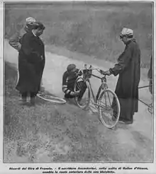 A man working on the front tire of a bicycle; three men are watching.