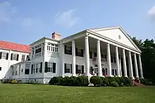 A two-story white house with red roof and columned porch.