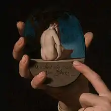 A hand holds an erotic medallion, while the paired hand points to it