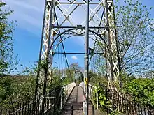 A view of the Howley Suspension bridge from the Victoria Park side facing towards Warrington Town Centre, which shows the main structure and suspension cables painted in black and white spanning the river Mersey.