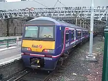 A purple colour train parked on a platform. The name of the company i.e. "First" is written on the sides. The last coach has a yellow paint on lower half with "first" and logo "f" written on it. It also has number 322 485 written on it.