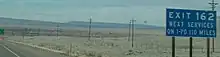 A blue sign against a desert landscape. The sign reads "Exit 162, next services on I-70 110 miles".